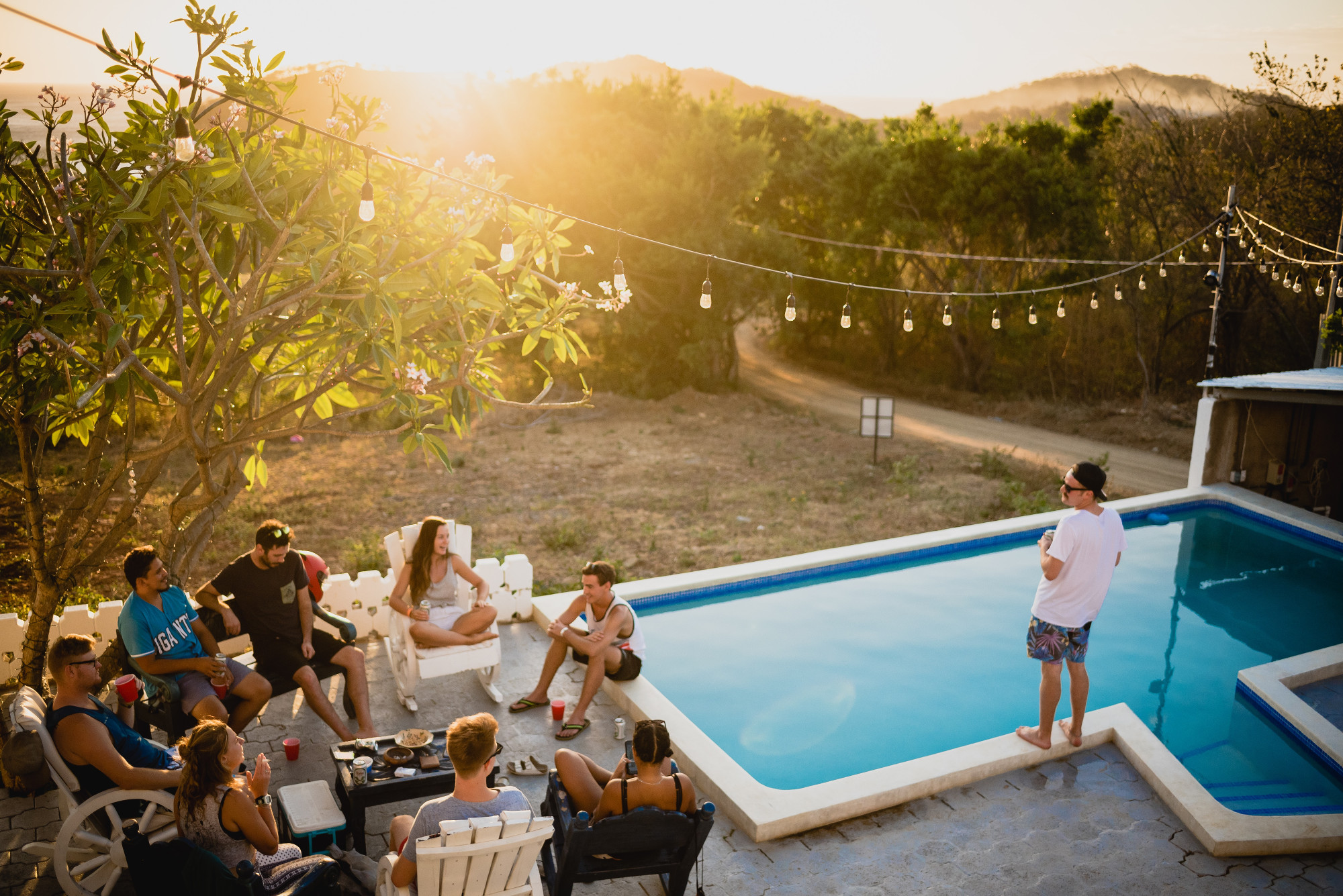 extérieur avec piscine et guirlandes lumineuses avec personnes assises qui boivent un verre